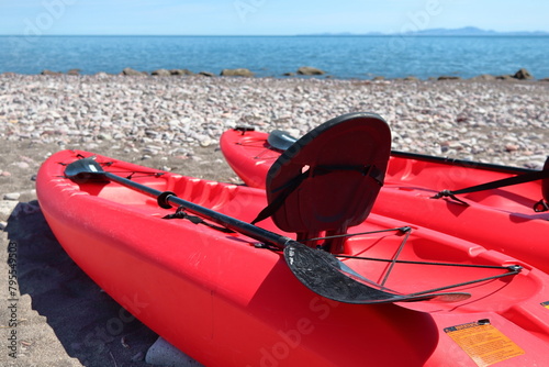 Recreational red kayak with paddles and hard plastic seat back, on the beach