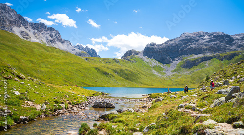 Hikers (unrecognizable people) admire the view of beautiful La Plagne lake in the French Alps. Peisey valley, Savoie, France. Summer active holidays in nature.