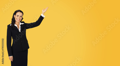 Happy smiling woman wear confident suit, showing at mock up slogan text empty blank place. Business ad concept. Isolated against orange yellow wall background. Wide banner image