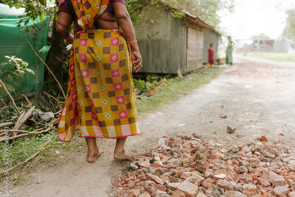old indian woman in traditional sari walking on dirt road in a village in rural India. Concept of poverty and infrastructure and India development old indian woman in traditional sari walking on dirt road in a village in rural India. Concept of poverty and infrastructure and India development