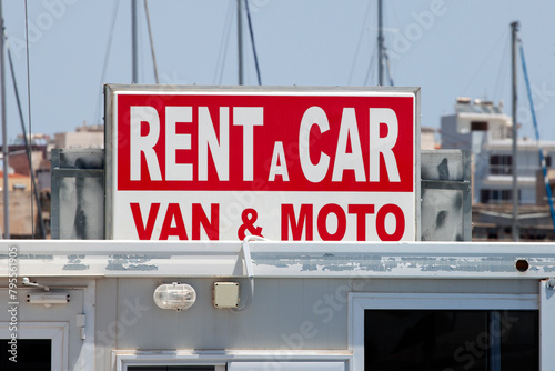 sign that says : rent a car , van and moto, with red and white letters . sunny day