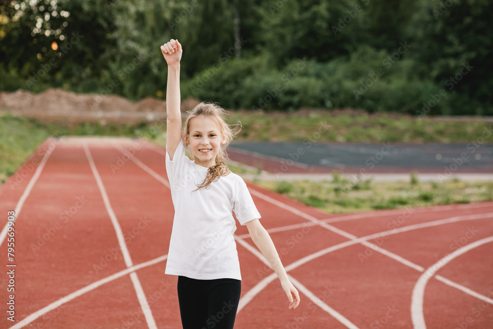 Cheerful pre-teen girl raises her hand up in victory on the running track. Sport and life accomplishment, teamwork, ,success concept Cheerful pre-teen girl raises her hand up in victory on the running track. Sport and life accomplishment, teamwork, ,success concept