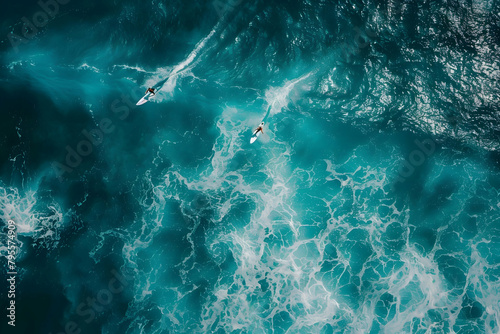 An aerial view of two surfers riding waves in the ocean, captured from above 