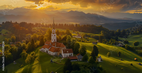 erial view of a traditional old church on a hill in a beautiful green valley with a forest and mountains at sunset photo