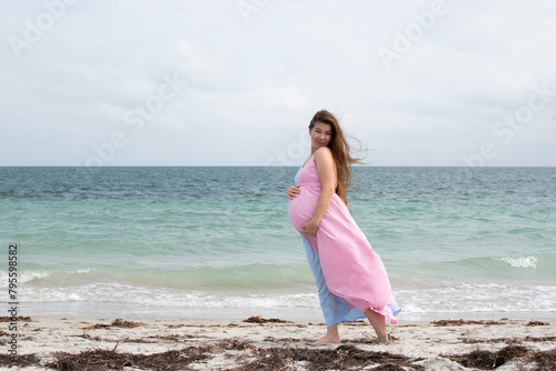 Pregnant Caucasian woman in a long dress near the ocean. Pregnant woman with long hair on a beach. happy pregnancy concept