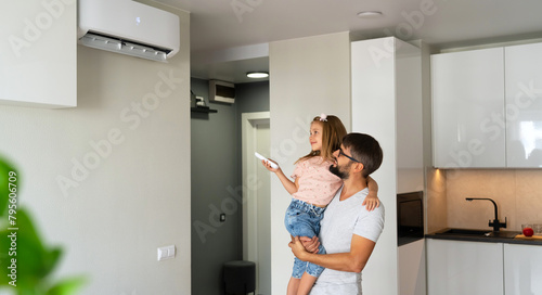 Father and little girl turn on air conditioner using remote control. Happy family adjust comfortable temperature of cooler system