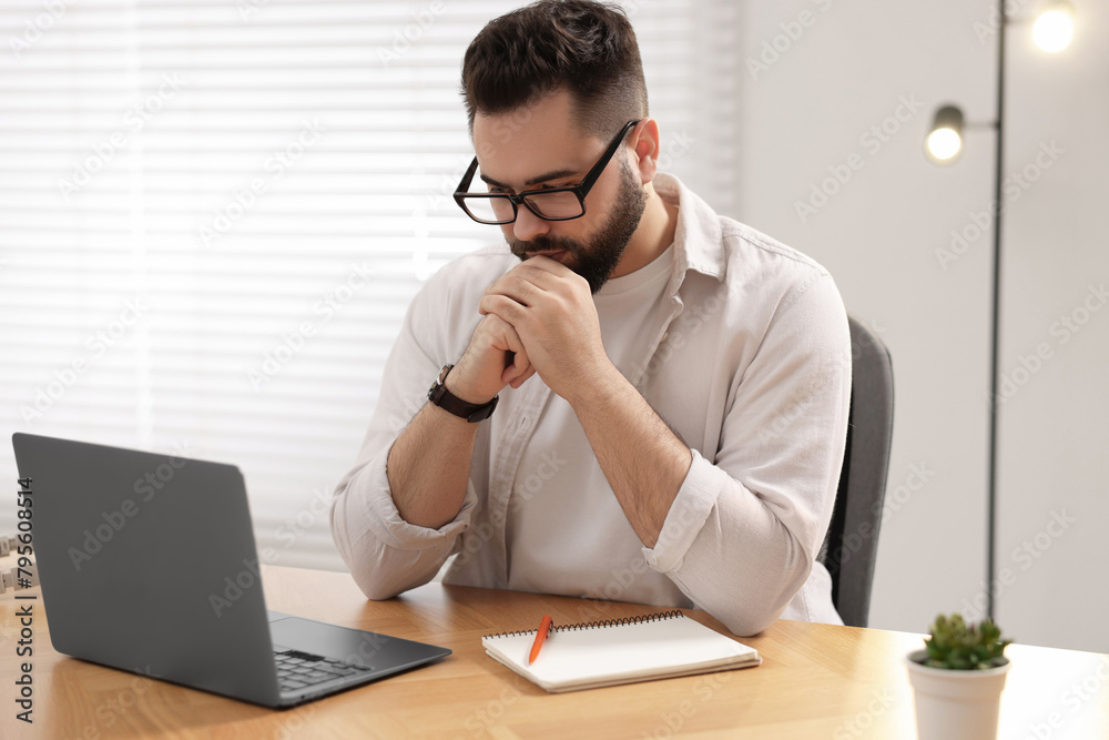 Young man in glasses watching webinar at table in room