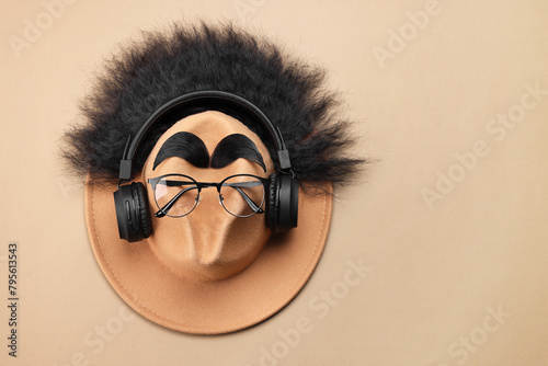 Man's face made of artificial hair, eyebrows, glasses and hat on beige background, top view. Space for text
