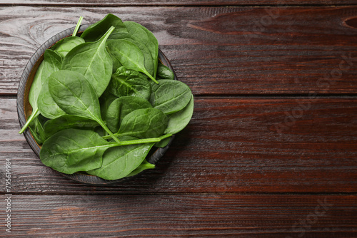 Fresh spinach leaves in bowl on wooden table, top view. Space for text