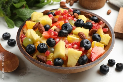 Delicious fruit salad in bowl, berries, fresh mint and nuts on white marble table, closeup