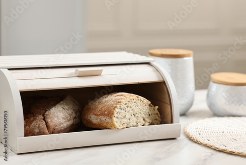 Wooden bread basket with freshly baked loaves on white marble table in kitchen photo