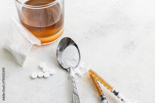 Narcotic substances in spoon, dope powder in transparent plastic bag, syringes with drugs dose, white pills and glass of alcohol drink on textured background. Concept of addiction and bad habits