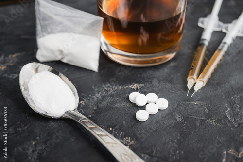 Narcotic substances in spoon, dope powder in transparent plastic bag, syringes with drugs dose, white pills and glass of alcohol drink on dark textured background. Concept of addiction and bad habits