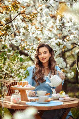aesthetic tea party in a blooming garden. portrait of a beautiful young woman drinking tea