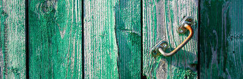 Iron handle on a wooden door. Rusty handle on a vertical plank door, side view. The paint on the old door boards has weathered with age