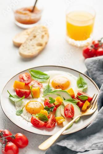 Healthy breakfast. Fried eggs and vegetables - cherry tomatoes, avocado slices, spinach leaves, sweet pepper and parsley in plate on the table © murziknata