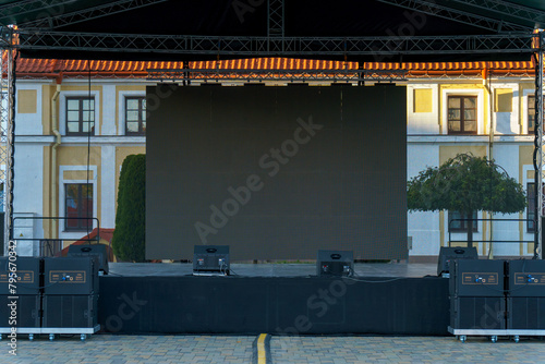 Large indoor outdoor stage for concerts. Professional sound and lighting equipment on stage. Monitor speakers  and big screen on stage.