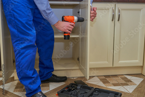 Фотография a carpenter installs a handle on a kitchen cabinet, work of a man repairing a ki