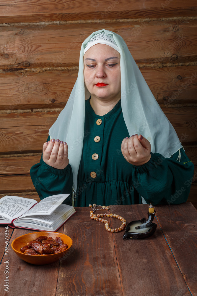 A Muslim woman at the table prays before the end of the Ramadan fast on the table with dates and rosary A Muslim woman at the table prays before the end of the Ramadan fast on the table with dates and rosary