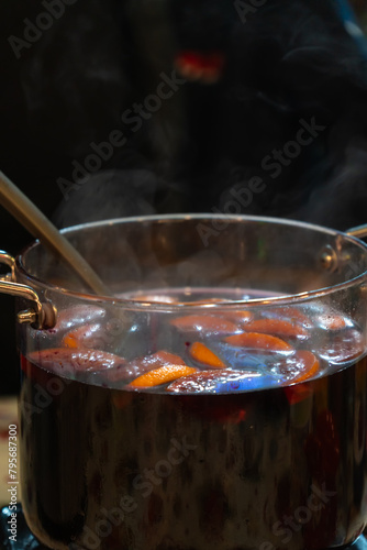 Close-up of a large glass pan with hot spicy mulled wine made from fruits and berries at an outdoor fair and festival. Vertical photo