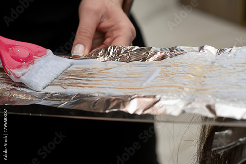 Beauty sphere. Hair coloring in a beauty salon. A master hairdresser-colorist dyes a client's brown hair blond. Apply lightening powder to hair onto foil using a pink brush. Close-up.