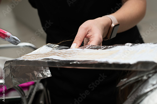 Beauty sphere. Hair coloring in a beauty salon. A master hairdresser-colorist dyes a client's brown hair blond. Apply lightening powder to hair onto foil using a pink brush. Close-up.