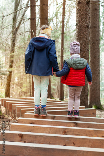 Zwei Kinder laufen auf Holzstamm im Wald. Kinder unterstützen sich gegenseitig bei gleichgewichtsübung auf Holzstämmen. Two children help each other to balance on logs. 