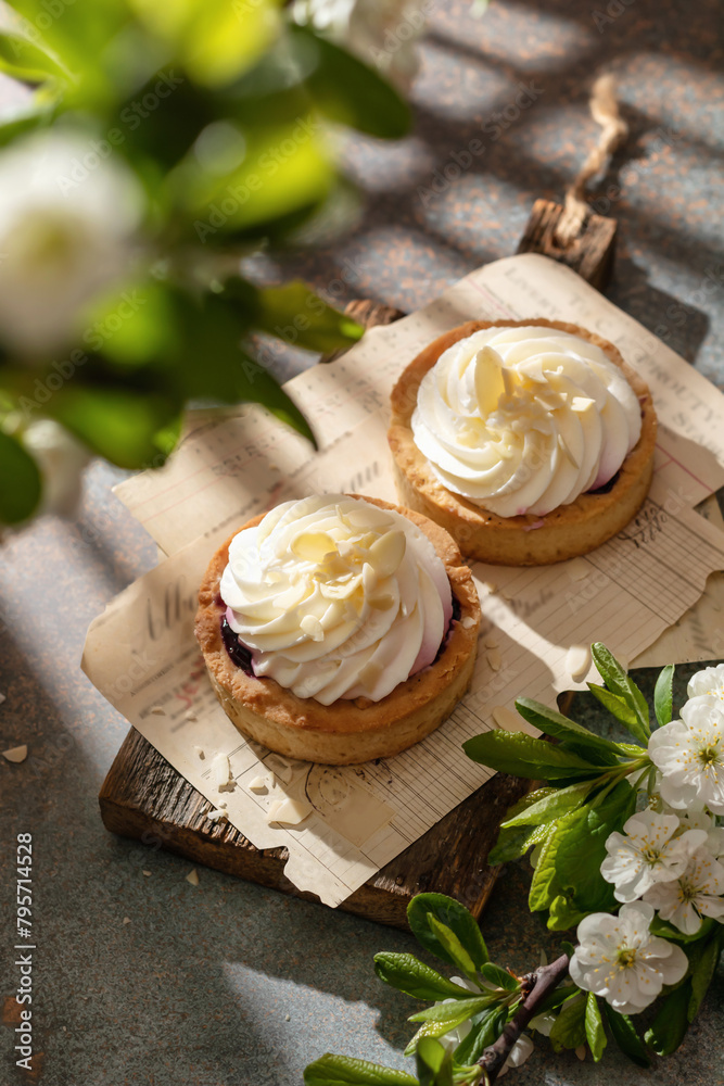 Sweet almond cream tarts on rustic wooden board in spring white flowers with beautiful morning shadows