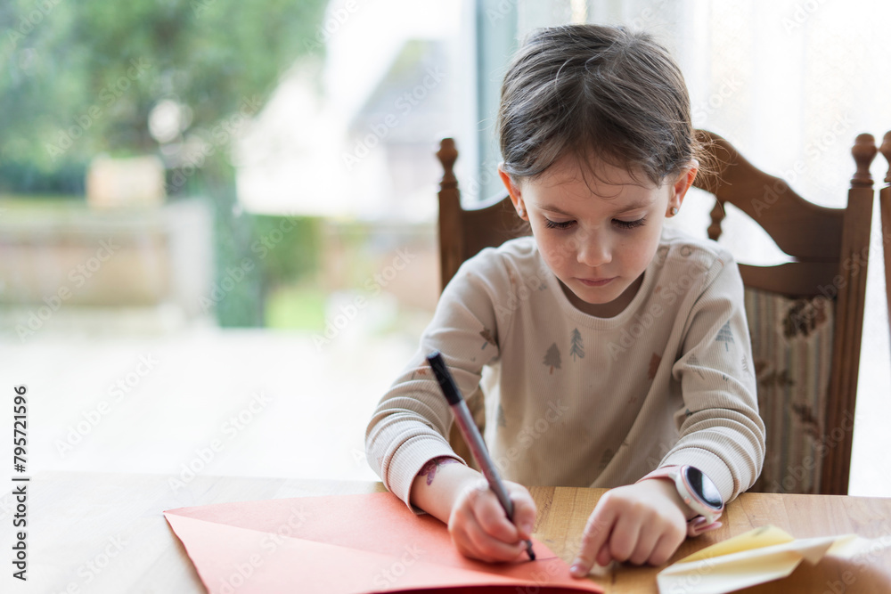 Little girl writing in a notebook while sitting at the table at home Little girl writing in a notebook while sitting at the table at home