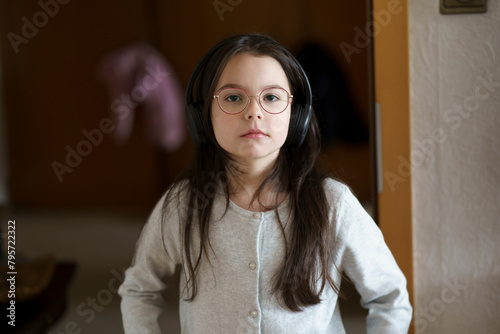 Portrait of a cute little girl with glasses and headphones at home