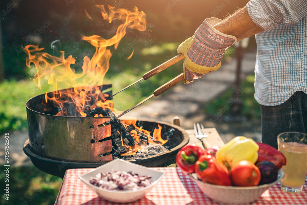 Fototapeta premium Unknown male person holding a grabbing tool while preparing barbecue outdoors. Fresh vegetables to grill.