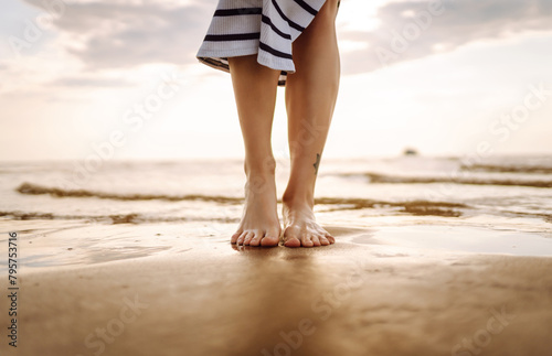 Slim female legs and feet walking along sea water waves on sandy beach. Pretty woman walks at seaside surf. The concept of relax, travel, freedom and summer vacation. © maxbelchenko