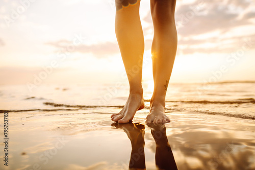 Slim female legs and feet walking along sea water waves on sandy beach. Pretty woman walks at seaside surf. The concept of relax, travel, freedom and summer vacation.