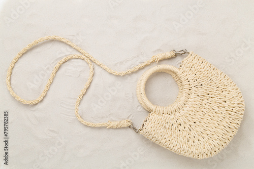 Straw bag on sand background, top view