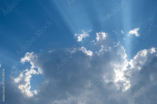 Sunbeams radiating through silver lined clouds in a vivid blue sky. Ideal for concepts of hope and inspiration.