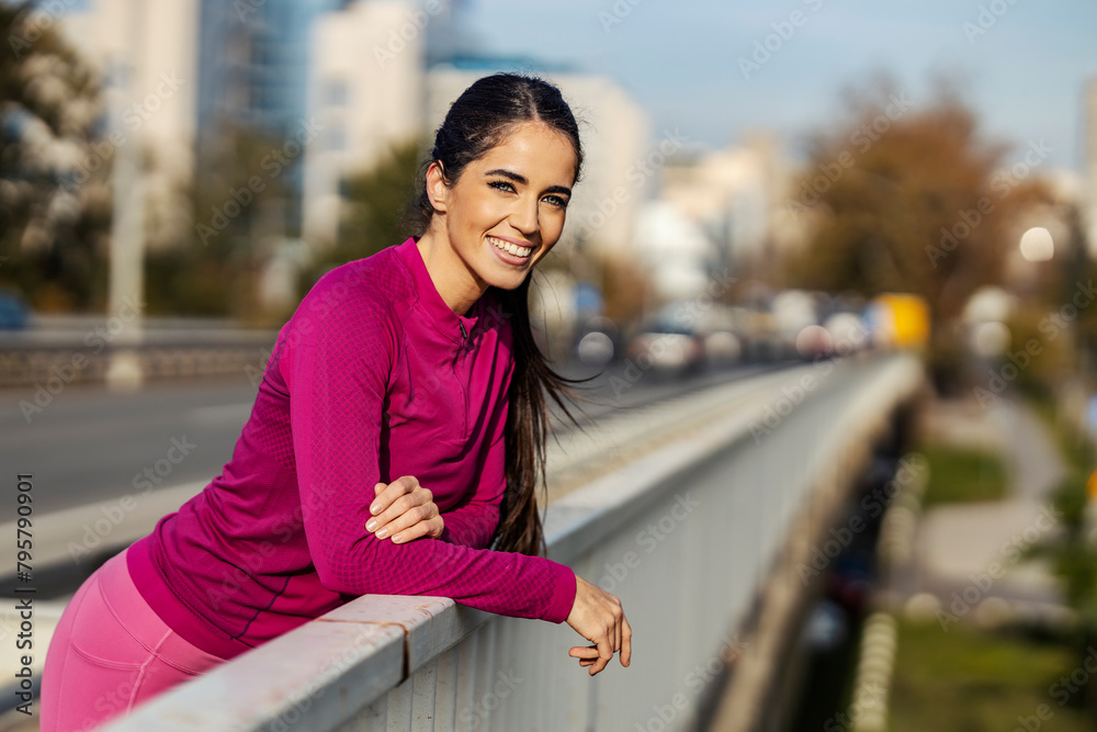 Portrait of a fit sportswoman leaning on fence and smiling at the camera.