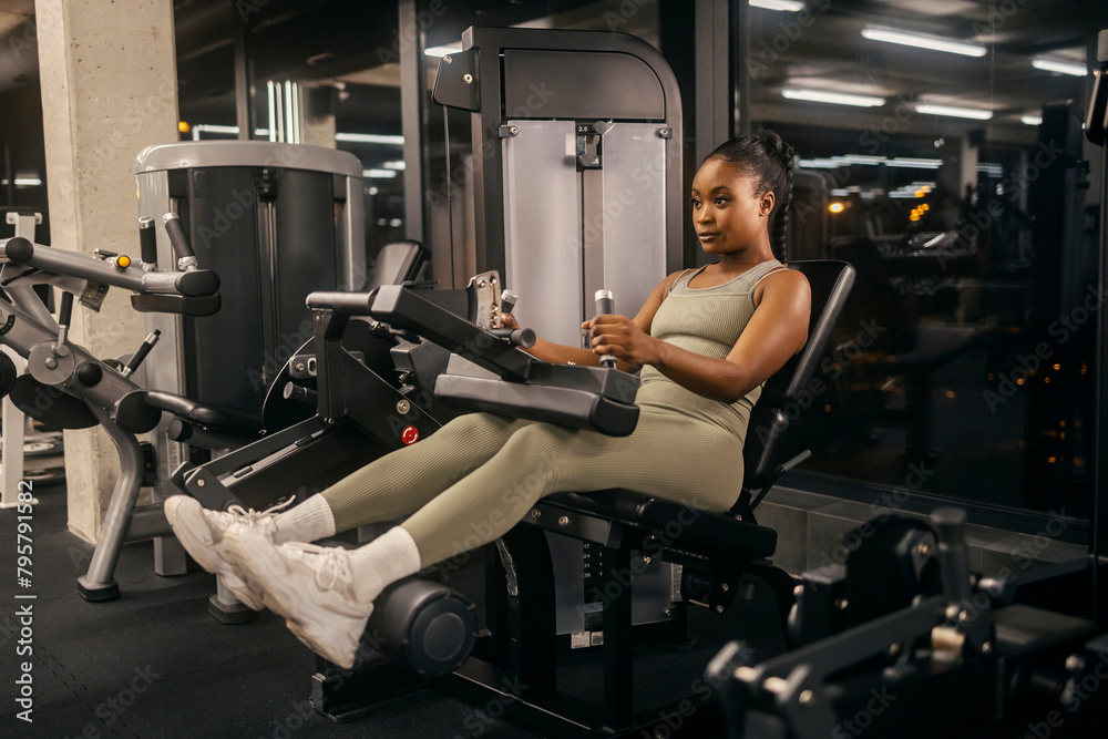 A strong black sportswoman doing workouts at seated leg curl machine at gym. A strong black sportswoman doing workouts at seated leg curl machine at gym.