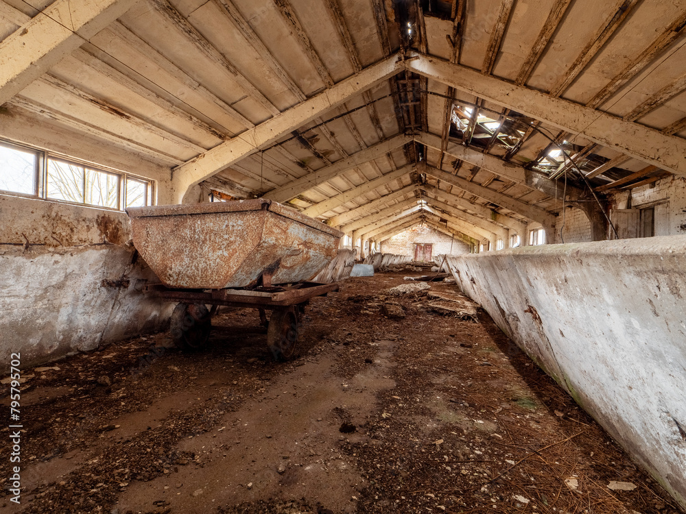 Scene inside old abandoned milk cow farm with feeders, windows and old equipment. Soviet union style collective farm. Cost of running agriculture business and economy effects on production. Scene inside old abandoned milk cow farm with feeders, windows and old equipment. Soviet union style collective farm. Cost of running agriculture business and economy effects on production.