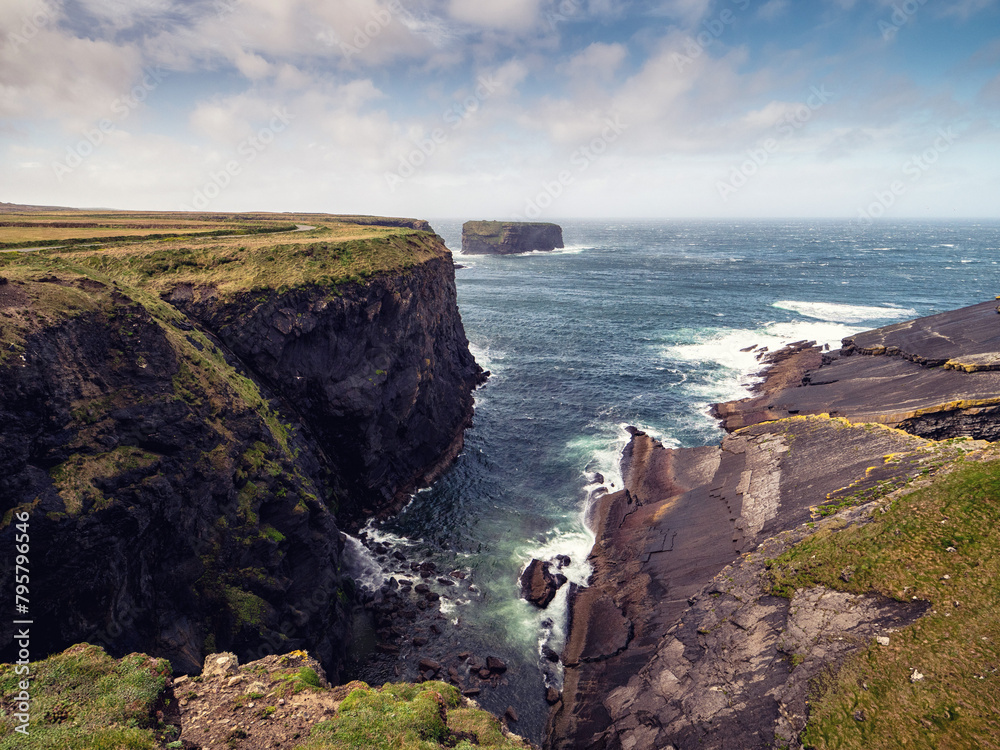 Kilkee cliff in county Clare, Ireland. Popular travel area with stunning nature scenery with green fields, ocean and dramatic sky. Irish landscape. Rough coast line. Warm sunny day.