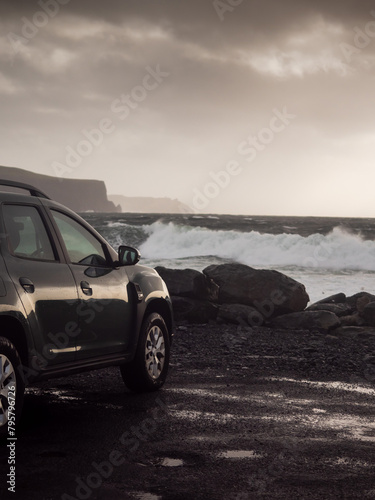 Car parked close to the ocean with view on amazing nature scene with powerful waves. Doolin area, county Clare, Ireland. Travel and tourism concept. Rented car trip theme. Rough Irish landscape photo