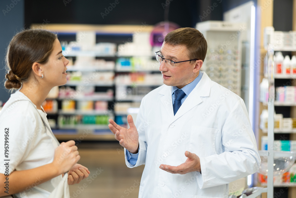 Pharmacist man communicates with girl visiting pharmacy, answers questions, provides advice and assistance