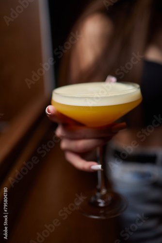 A woman holds a cocktail in her hand  with her fingers wrapped around the glass