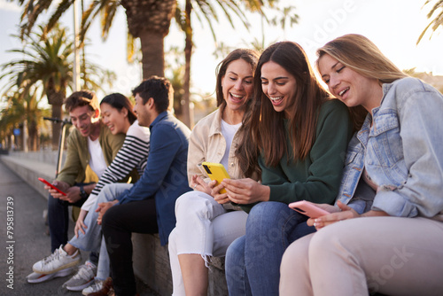 Large and diverse group of generation z friends smiling sitting on street using and looking mobiles phones. Addiction of technology and social networks of young happy people sunny day outdoors photo