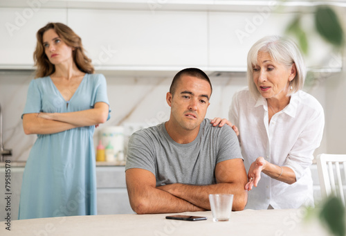 Adult woman during family quarrel with elderly woman and adult man in kitchen