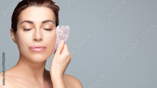 Woman Using Rose Quartz Gua Sha for Facial Rejuvenation. Close up with copy space
