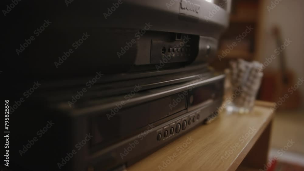 Tilt closeup of hands of mischievous gen Y kid putting cassette with Zombie Attack movie into video tape recorder and switching on TV, nostalgic childhood in 90s