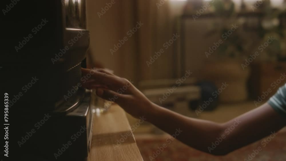 Side handheld footage of naughty gen Y African American boy taking cassette out of schoolbag, putting it into tape video recorder and switching on retro TV watching horror movie while alone at home