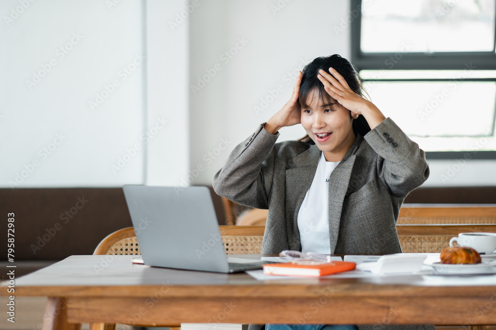 Office worker expresses shock with hands on head while staring at a laptop screen, a scene of unexpected news or error at work.