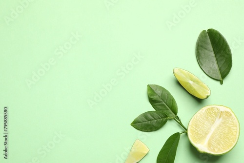 Cut fresh ripe limes with leaves on light green background, flat lay