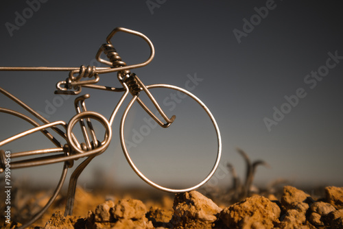 A miniature metal bicycle against a dark grey blue sky. Toy fake souvenir hand made craft mini bike in a wild. Mountain biking concept. The wheel of a bike stands on a rock surface. World bicycle day. photo